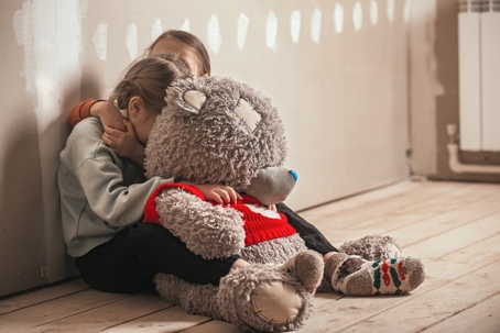 scared children hiding behind large teddy bear