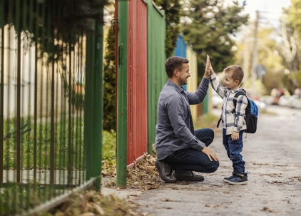 A father is giving high five to his kindergartener on school entrance.