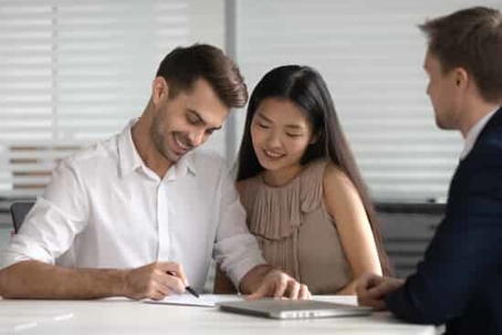 A young couple smiling and signing a contract