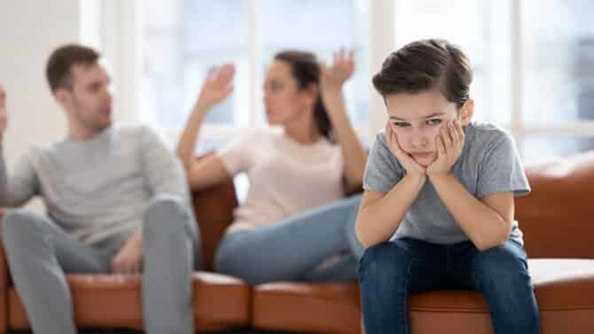 boy with his head in his hands while his parents are fighting behind him